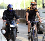 Un ciclista con casco circula entre varios vehículos, como motos y coches, por las calles de una ciudad