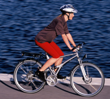 Una chica circulando en bicicleta y con casco por un carril bici paralelo a un estanque