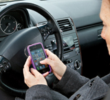 Mujer joven sentada frente al volante de un coche y manipulando un teléfono móvil