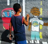 Niño brasileño pintando una pared con dibujos de un coche y una carretera